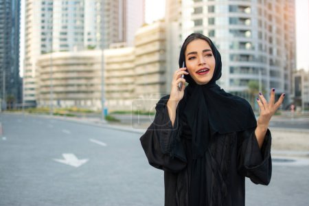 Foto de Mujer emiratí del Medio Oriente hablando por teléfono móvil mientras camina por la calle - Imagen libre de derechos