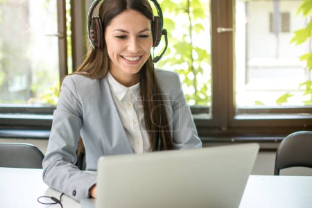 Foto de Joven mujer de negocios con auriculares que trabajan en el ordenador portátil en la oficina moderna. - Imagen libre de derechos