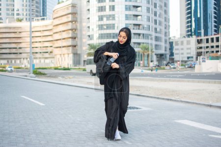 Jeune femme musulmane dans la tradition vêtements Abaya portant sac de sport et bouteille d'eau va à la salle de gym