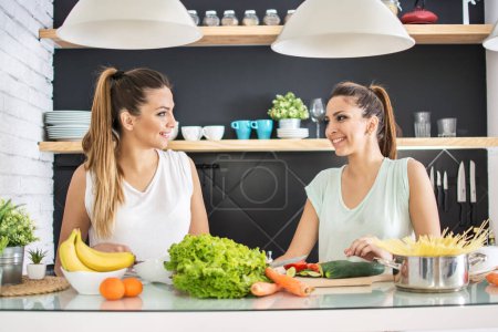 Téléchargez les photos : Joyeuses jeunes sœurs jumelles préparant ensemble une salade de légumes bio pour le déjeuner dans la cuisine - en image libre de droit