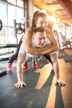 Photo for Muscular man doing push ups with woman on back in gym - Royalty Free Image