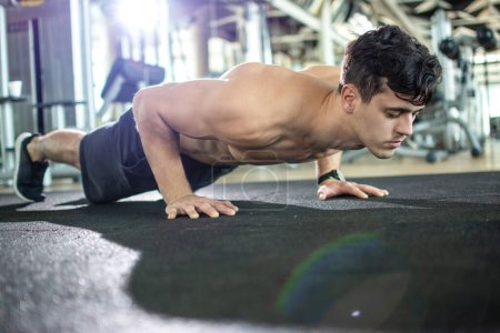 Téléchargez les photos : Jeune homme athlétique faisant des pompes dans la salle de gym - en image libre de droit