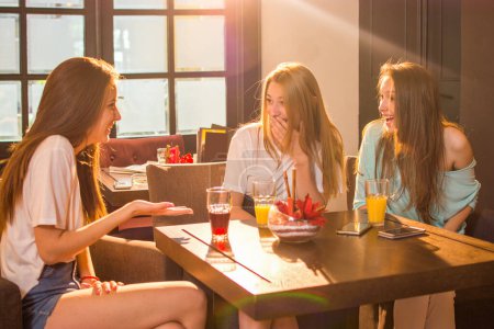 Foto de Tres hermosas mujeres jóvenes hablando y sonriendo mientras beben jugos en el restaurante - Imagen libre de derechos