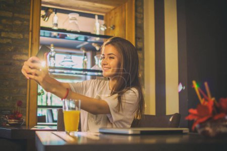 Foto de Sonriente adolescente tomando una selfie en el teléfono móvil en la cafetería. - Imagen libre de derechos