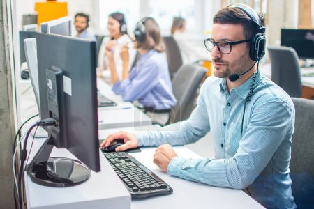 Photo for Focused middle aged handsome man in formal shirt and headset working on computer in call center agency. - Royalty Free Image