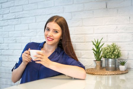 Photo for Smiling young woman having a cup of coffee at home - Royalty Free Image