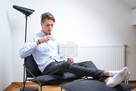 Téléchargez les photos : Jeune homme prenant une tasse de café tout en se relaxant dans sa chambre - en image libre de droit