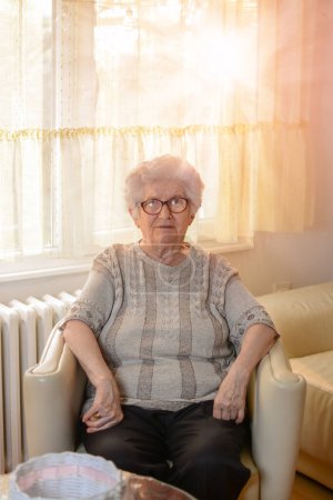 Téléchargez les photos : Portrait de vieille femme assise sur un fauteuil et relaxante à la maison. - en image libre de droit