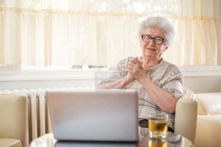 Téléchargez les photos : Femme âgée émotionnelle ayant un appel vidéo avec les petits-enfants via un ordinateur portable. - en image libre de droit