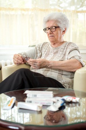Confused senior woman with eyeglasses reading pill labels.