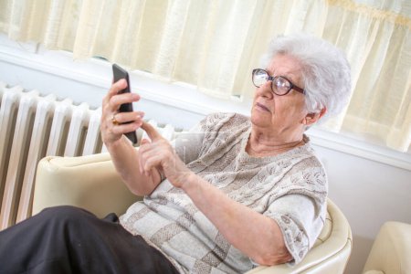 Téléchargez les photos : Femme âgée confondue utilisant la télécommande pour changer de canal. - en image libre de droit