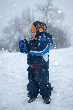 Téléchargez les photos : Portrait complet d'un petit garçon debout sur la neige dans un parc d'hiver - en image libre de droit