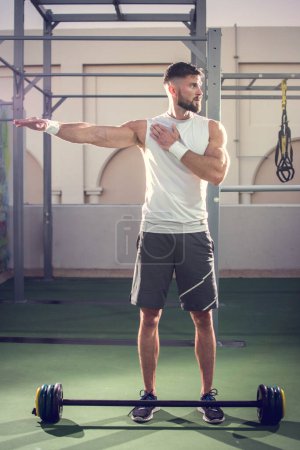 Foto de Handsome man stretching before weightlifting in gym. - Imagen libre de derechos