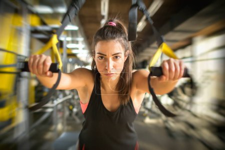 Photo for Sporty girl working out on suspension straps in gym. - Royalty Free Image