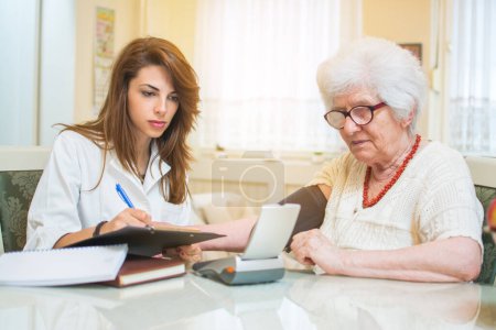 Foto de Enfermera escribiendo a portapapeles los resultados de la medición de la presión arterial del paciente mayor femenino - Imagen libre de derechos
