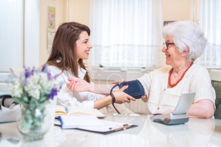 Foto de Enfermera midiendo la presión arterial de la mujer mayor en casa - Imagen libre de derechos