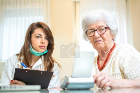 Foto de Enfermera con portapapeles que escribe los resultados de la medición de la presión arterial del paciente mayor femenino - Imagen libre de derechos