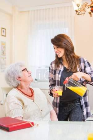 Granddaughter pouring fresh orange juice to her grandmother. Family care concept