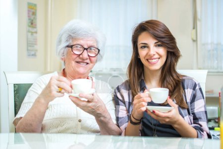Téléchargez les photos : Grand-mère et petite-fille assises à table et buvant du café - en image libre de droit