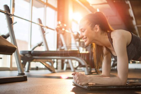 Téléchargez les photos : Vue latérale de belle femme sportive faisant de l'exercice de planche sur tapis à la salle de gym. - en image libre de droit