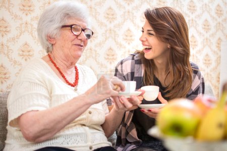 Téléchargez les photos : Joyeux petite-fille et sa grand-mère ayant ensemble tasses à café à la maison - en image libre de droit