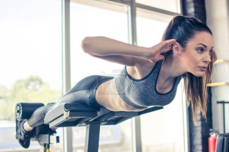 Schöne fitte Frau macht Rückenstreckgymnastik auf Fitnessgerät im Fitnessstudio