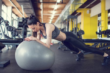 Téléchargez les photos : Sporty jeune femme faire pousser vers le haut sur la balle en forme à la salle de gym - en image libre de droit