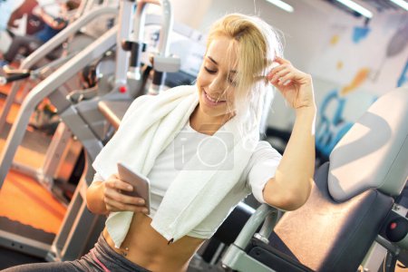 Photo for Attractive blonde girl using phone in gym. - Royalty Free Image