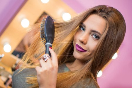 Close up portrait of beautiful young woman hairbrushing hair with brush at home.