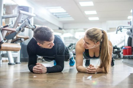 Foto de Joven mujer deportiva y hombre haciendo ejercicios de tablón juntos en el gimnasio. - Imagen libre de derechos