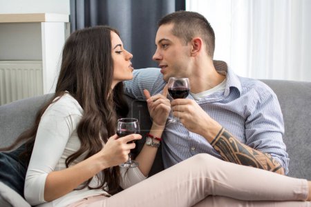 Téléchargez les photos : Beau jeune couple amoureux assis près de l'autre et boire du vin rouge
. - en image libre de droit