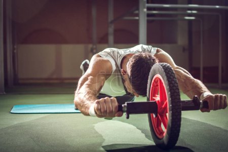 Foto de Entrenamiento de deportista guapo con rodillo abdominal en gimnasio. - Imagen libre de derechos