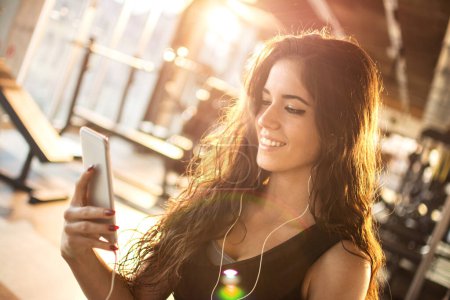 Photo for Sporty girl listening to music on smart phone at gym. - Royalty Free Image