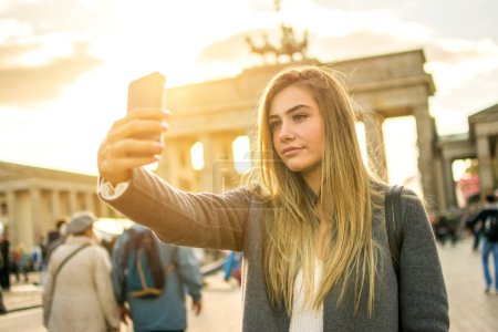 Foto de Hermosa joven rubia tomando selfie frente a la Puerta de Brandeburgo en la ciudad de Berlín, Alemania. - Imagen libre de derechos