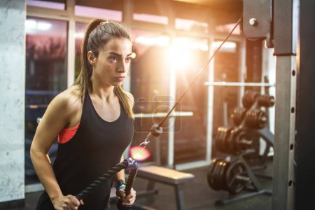 Fitness woman exercising on pull down machine at gym.
