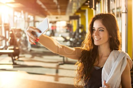Photo for Young sporty woman taking a selfie with mobile phone for social networks at gym. - Royalty Free Image
