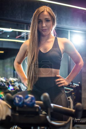Téléchargez les photos : Portrait de belle sportive mince aux cheveux longs posant sur un vélo d'appartement en salle de gym. - en image libre de droit