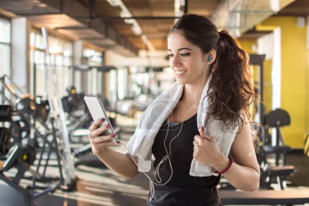 Téléchargez les photos : Femme sportive avec écouteurs utilisant un smartphone pour écouter des chansons préférées dans la salle de gym. - en image libre de droit