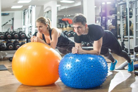 Foto de Pareja deportiva en posición de tabla haciendo ejercicio sobre bolas de fitness en el gimnasio. - Imagen libre de derechos
