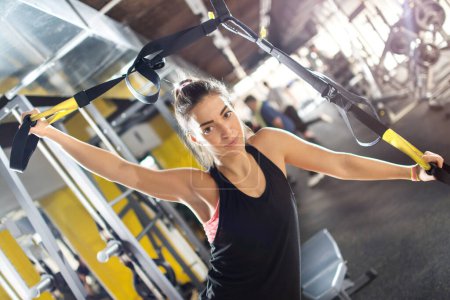 Photo for Young woman doing exercises with suspension straps at gym. - Royalty Free Image