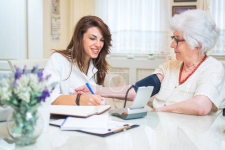 Photo for Nurse with clipboard writing results of blood pressure measurement of female senior patient - Royalty Free Image