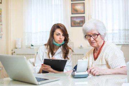 Foto de Cuidador midiendo la presión arterial de la mujer mayor en el hogar - Imagen libre de derechos