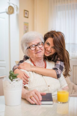 Photo for Beautiful cheerful teenage girl hugging her old grandmother - Royalty Free Image