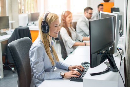 Photo for Smiling agent woman with headsets helping a customer accompanied with her team in call center - Royalty Free Image