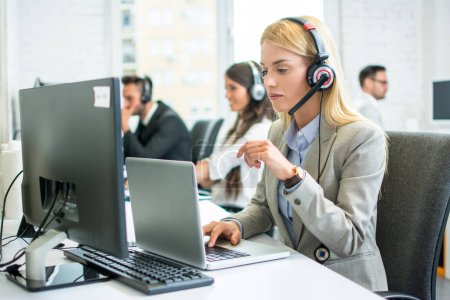 Téléchargez les photos : Femme d'affaires blonde pensive avec casque de travail sur ordinateur portable dans le centre d'appel - en image libre de droit