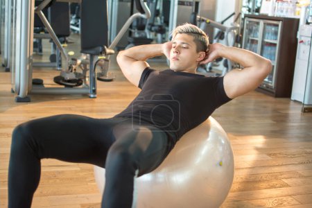Photo for Handsome sportsman doing crunches on fitness ball at gym. - Royalty Free Image