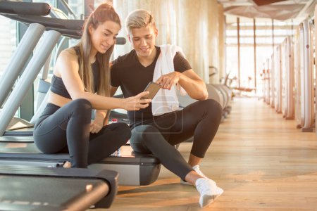 Téléchargez les photos : Couple sportif vérifiant les médias sociaux sur smartphone pendant la pause d'exercice à la salle de gym. - en image libre de droit