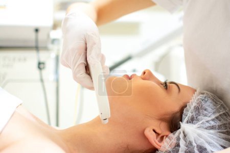 Téléchargez les photos : Esthéticienne appliquant un traitement avec un appareil moderne sur le cou de la jeune femme au salon de spa - en image libre de droit