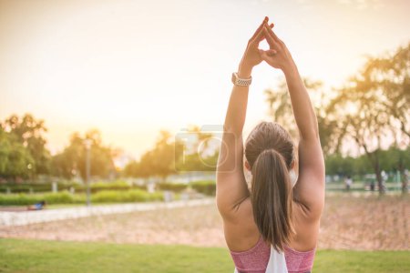 Photo for Back view of sporty woman practicing yoga in the park at sunset. Copy space available - Royalty Free Image