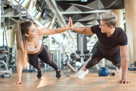 Photo for Happy sporty young couple doing push-ups exercise and giving high five each other in gym - Royalty Free Image